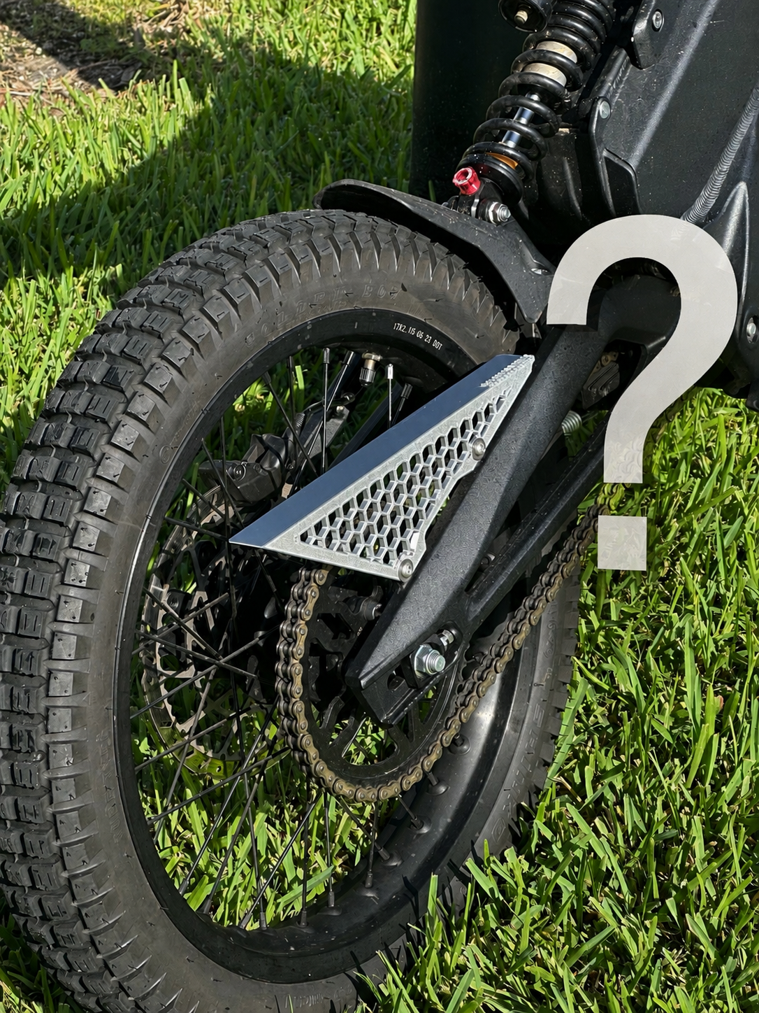 Mystery Chain Guard - X3A 3D-printed honeycomb chain guard fitted to an electric dirt bike, with a question mark overlay indicating the design is a surprise